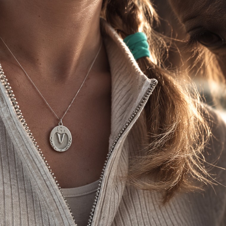 Sterling silver hoofprint pendant worn beside her horse in golden light